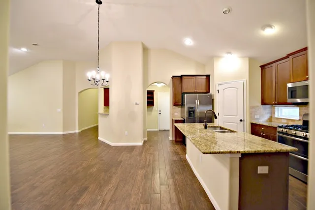 a kitchen with kitchen island granite countertop a stove a sink a refrigerator and a wooden floor