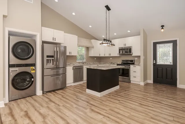 a kitchen with stainless steel appliances granite countertop a refrigerator a sink dishwasher a stove and white cabinets with wooden floor