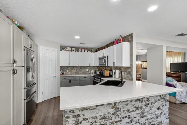 a kitchen with kitchen island a stove a refrigerator a oven a sink a dining table and chairs with wooden floor