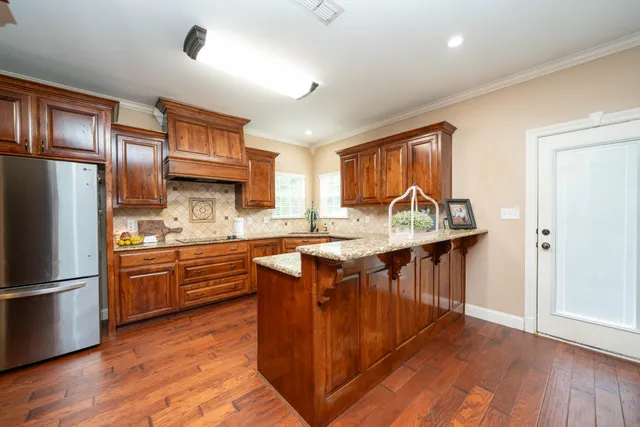 a kitchen with stainless steel appliances granite countertop a refrigerator a sink dishwasher a stove and white countertops with wooden floor