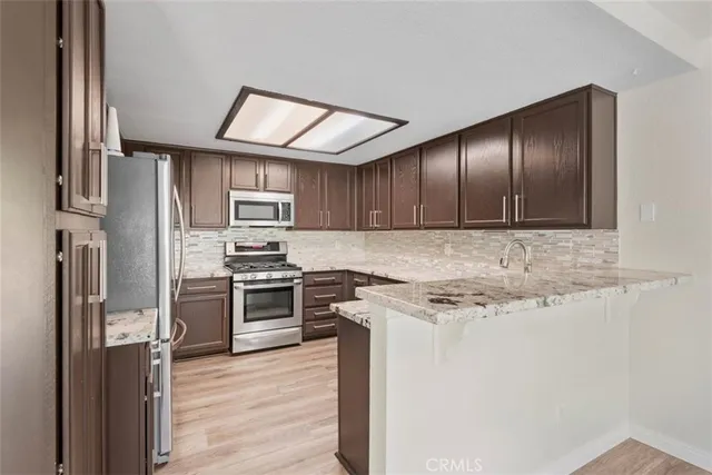 a kitchen with stainless steel appliances granite countertop a stove top oven a refrigerator and a sink with wooden floor