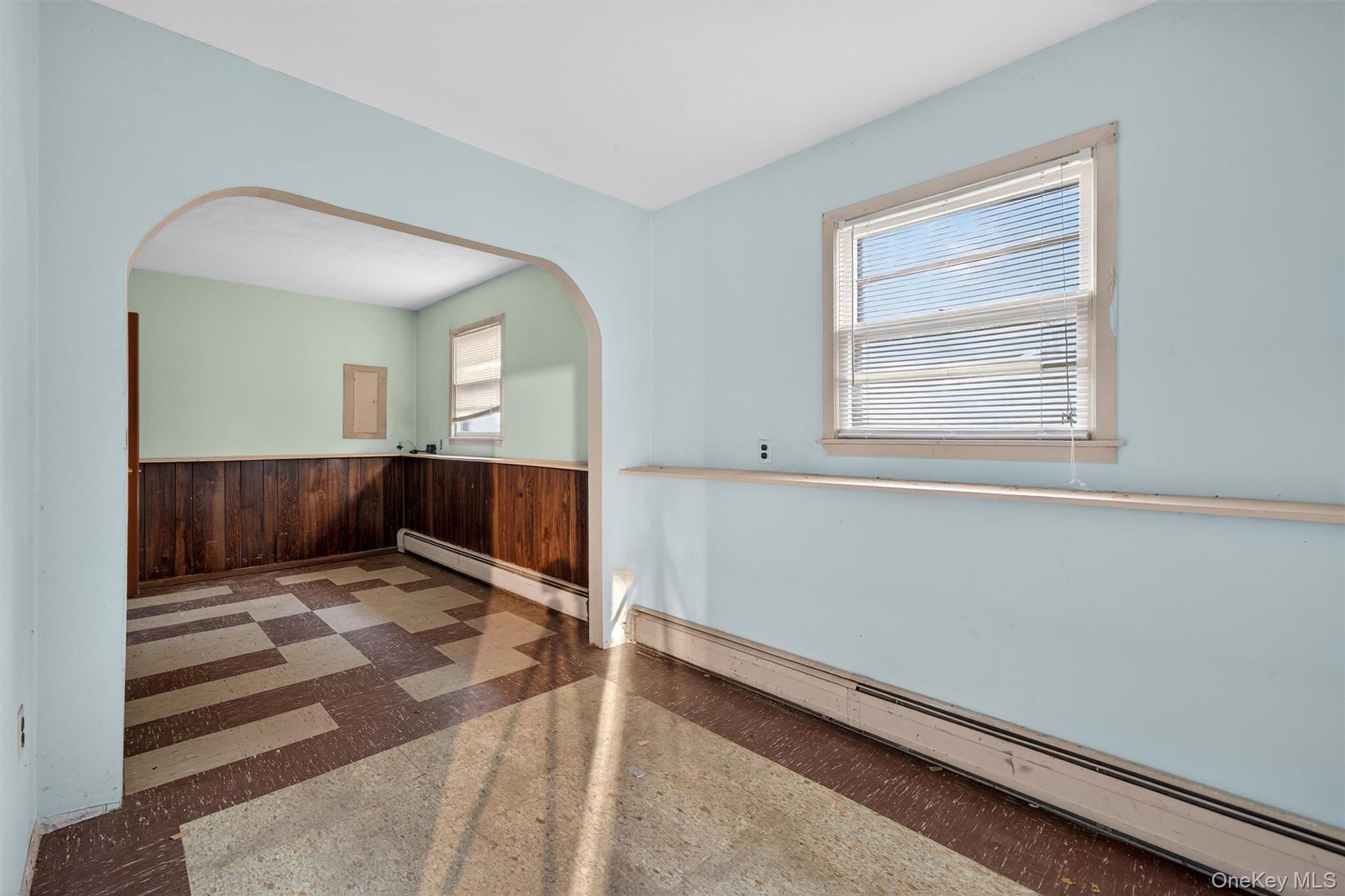 53 Mallory Road Spring Valley, NY 10977 - Photo 25 of 33 Empty room with a baseboard radiator, dark floors, wooden walls, arched walkways, and a wainscoted wall