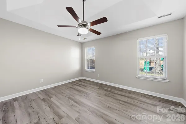 an empty room with wooden floor fan and windows