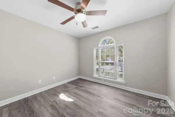 an empty room with wooden floor chandelier fan and windows