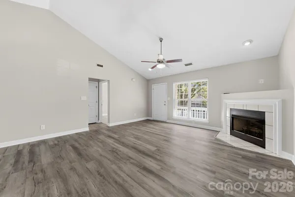 a view of an empty room with wooden floor fireplace and a window