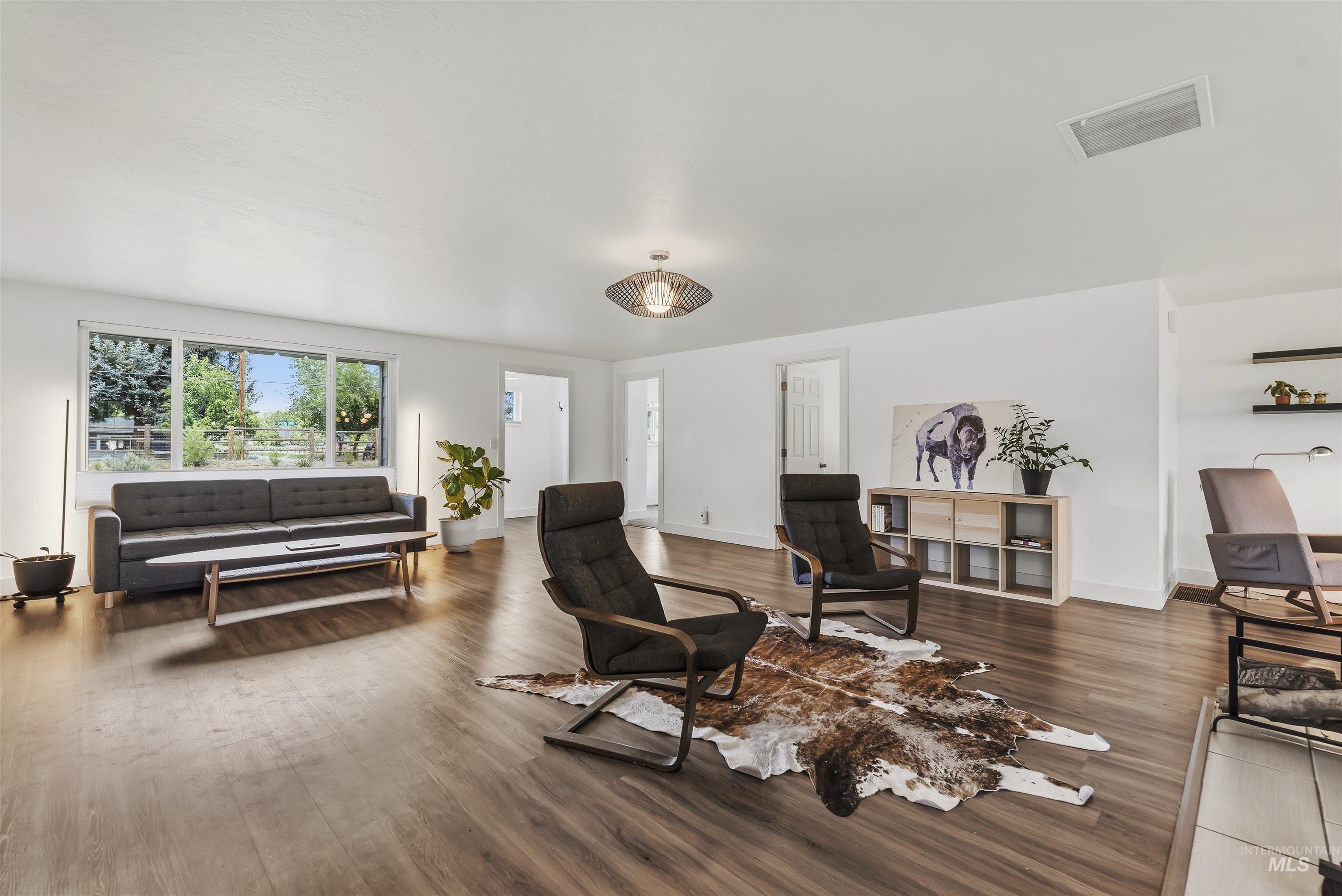 355 East Beacon Light Road Eagle, ID 83616 - Photo 7 of 47 Spacious living area featuring wood-finish flooring, white walls, and a large window overlooking mature landscaping
