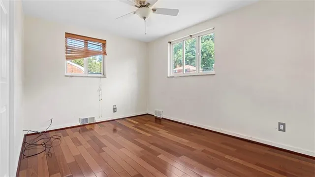 an empty room with wooden floor ceiling fan and windows