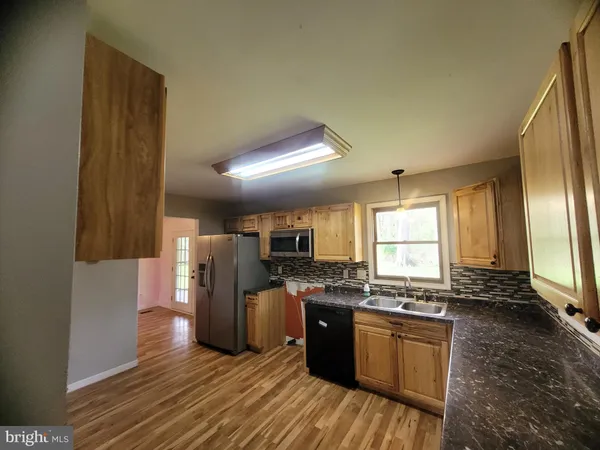 a kitchen with stainless steel appliances granite countertop a stove a sink dishwasher a refrigerator white cabinets and wooden floor