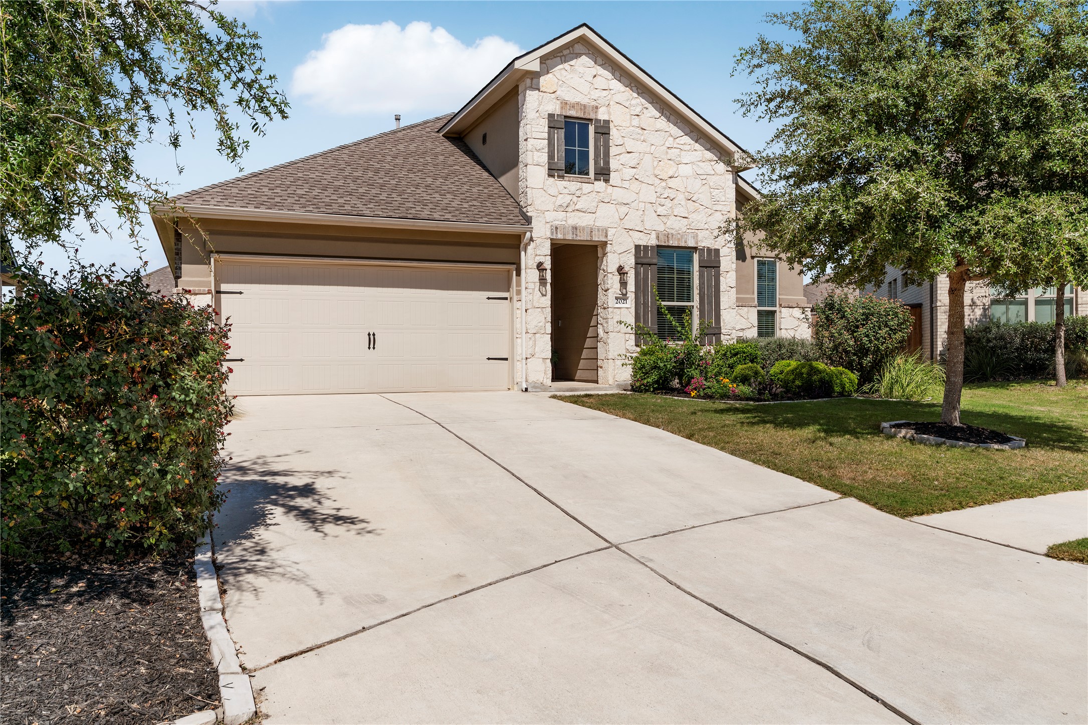 2021 Josiah Cove Leander, TX 78641 - Photo 2 of 35 View of front of property featuring stone siding, driveway, a garage, a front lawn, and roof with shingles