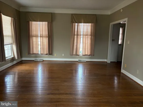 an empty room with wooden floor and windows with curtains