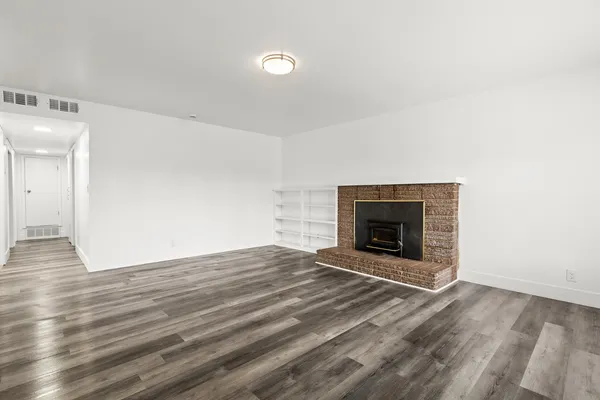 a view of an empty room with wooden floor and a fireplace