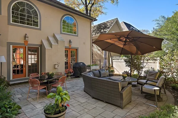 a view of a patio with couches table and chairs under an umbrella with large trees