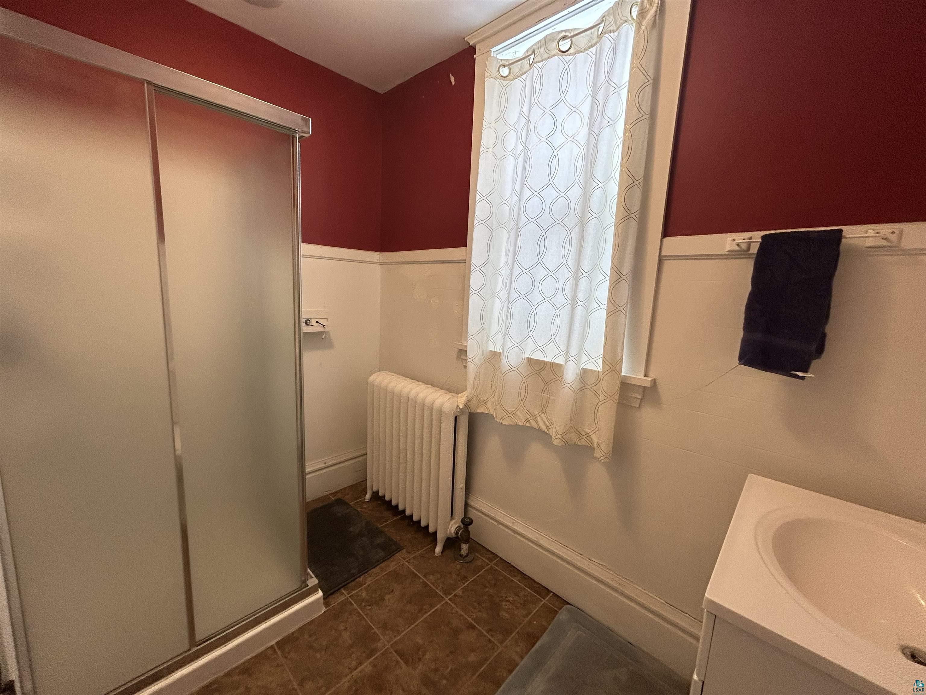 1723 East 4th Street Duluth, MN 55812 - Photo 12 of 47 Full bathroom featuring vanity, a shower stall, radiator, dark tile patterned flooring, and a wainscoted wall