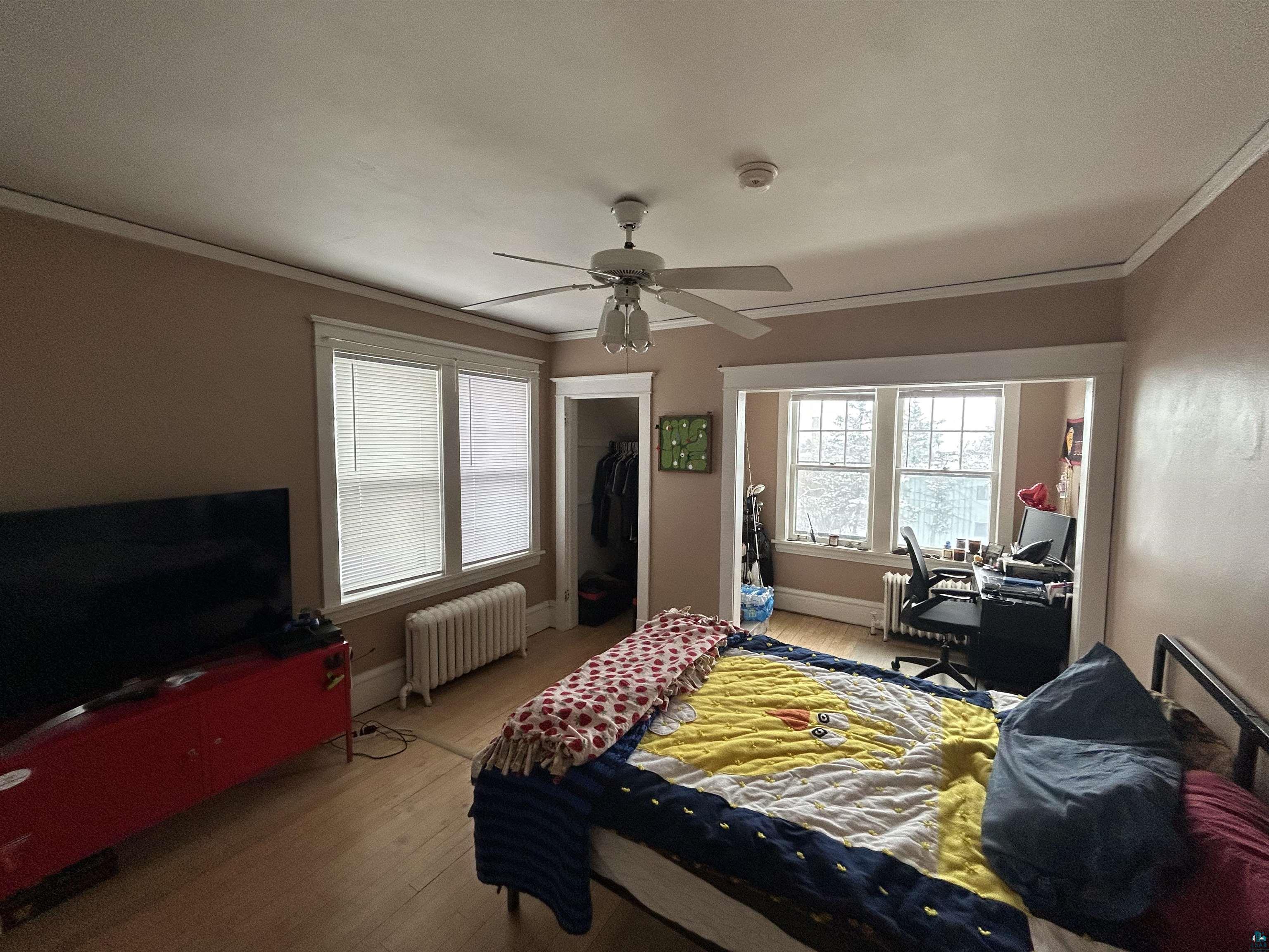 1723 East 4th Street Duluth, MN 55812 - Photo 19 of 47 Bedroom featuring radiator, light wood-style flooring, a closet, ornamental molding, and a ceiling fan