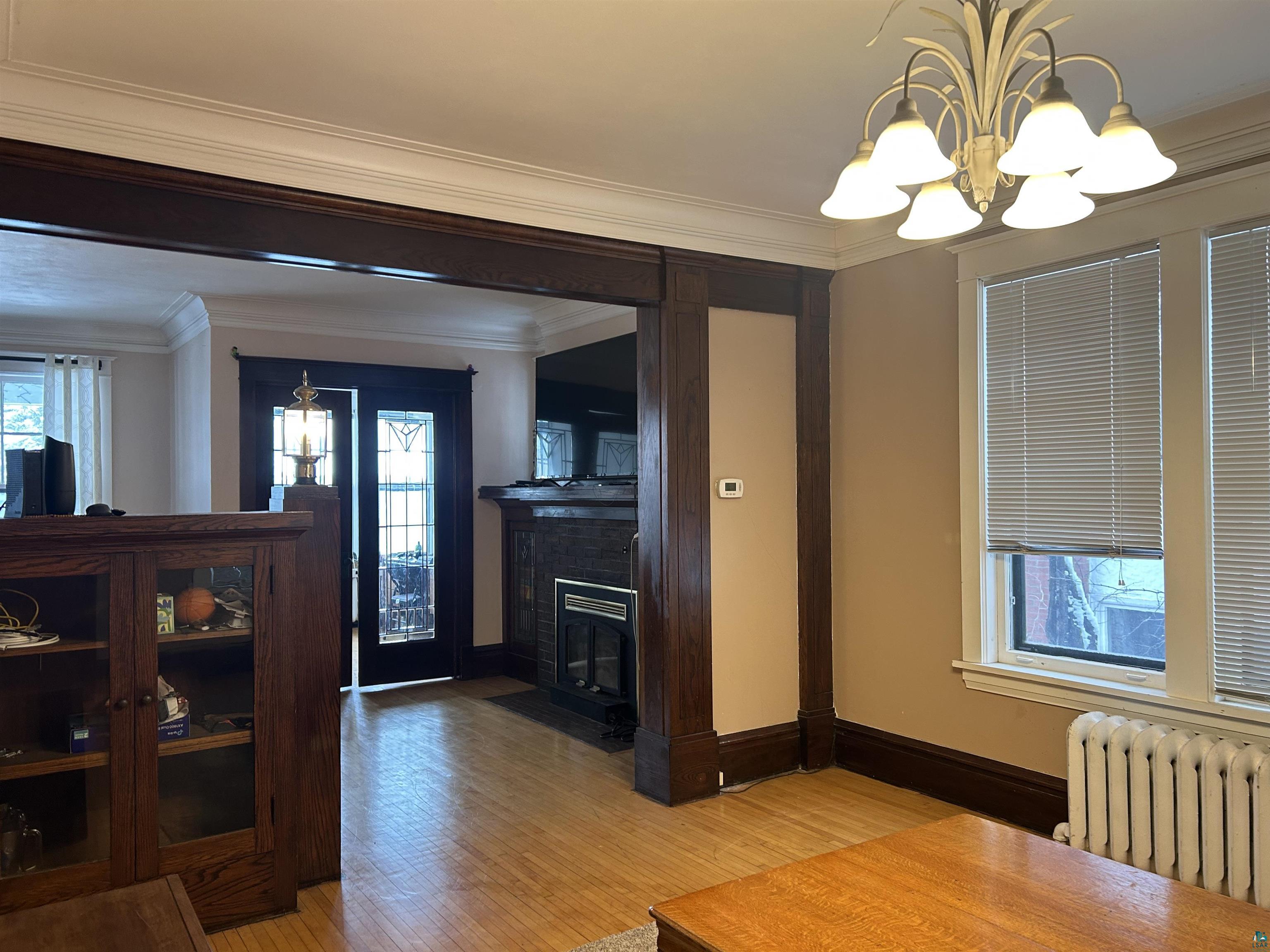 1723 East 4th Street Duluth, MN 55812 - Photo 35 of 47 Dining room featuring ornamental molding, radiator, light wood-style flooring, a chandelier, and a brick fireplace