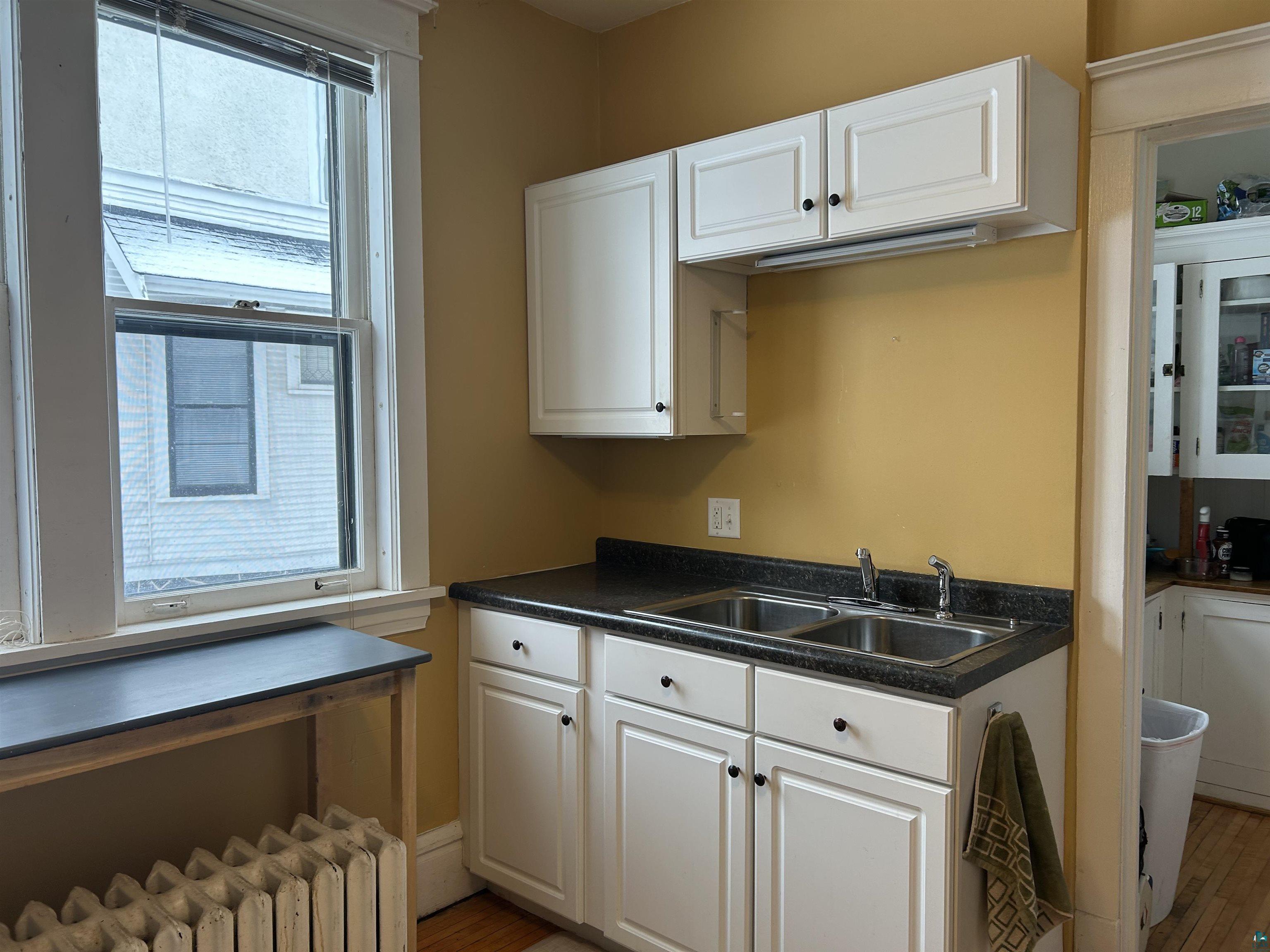 1723 East 4th Street Duluth, MN 55812 - Photo 7 of 47 Kitchen featuring white cabinets, radiator, dark countertops, and light wood-style floors