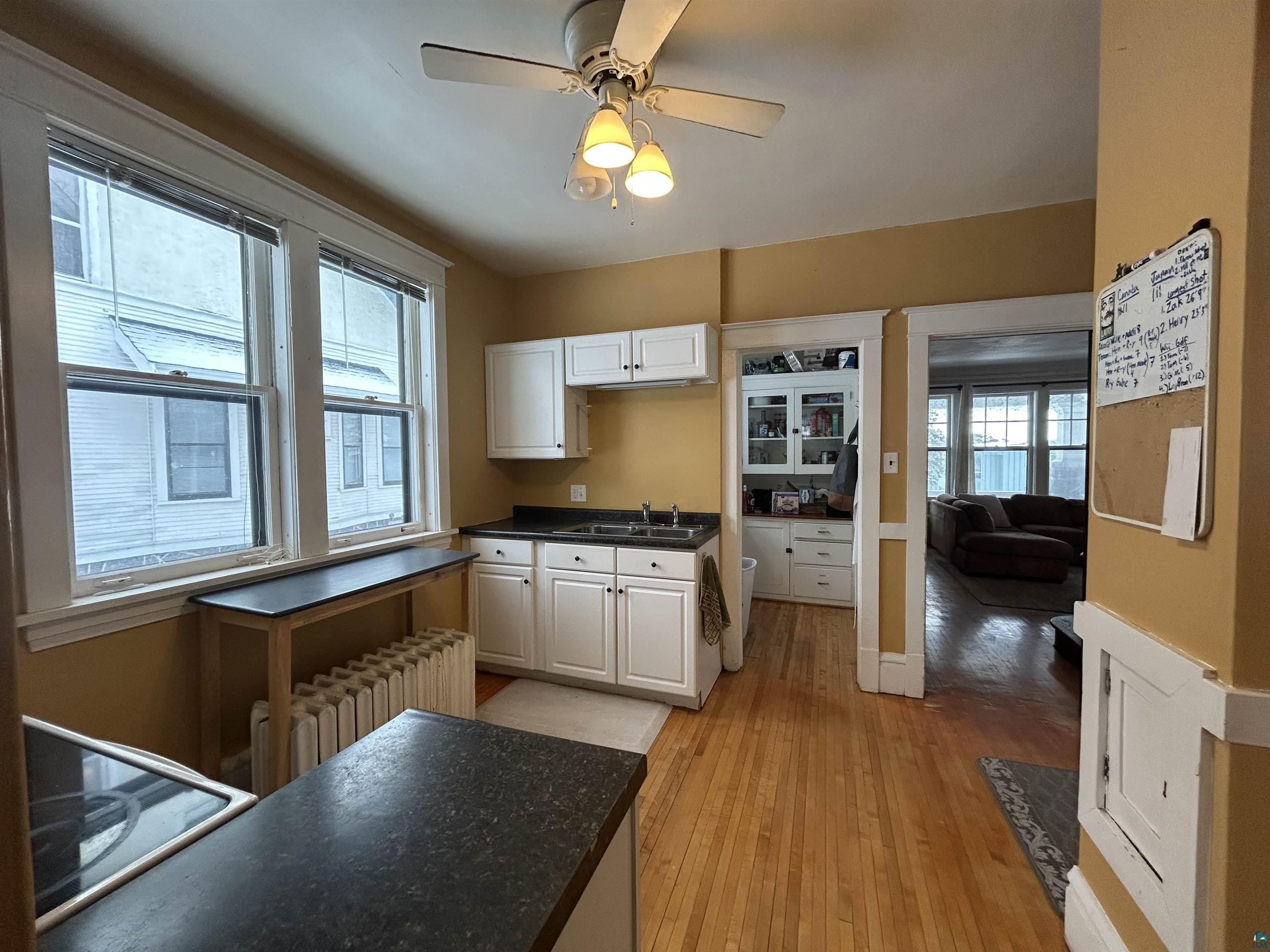 1723 East 4th Street Duluth, MN 55812 - Photo 9 of 47 Kitchen with dark countertops, radiator, electric stovetop, white cabinets, and ceiling fan