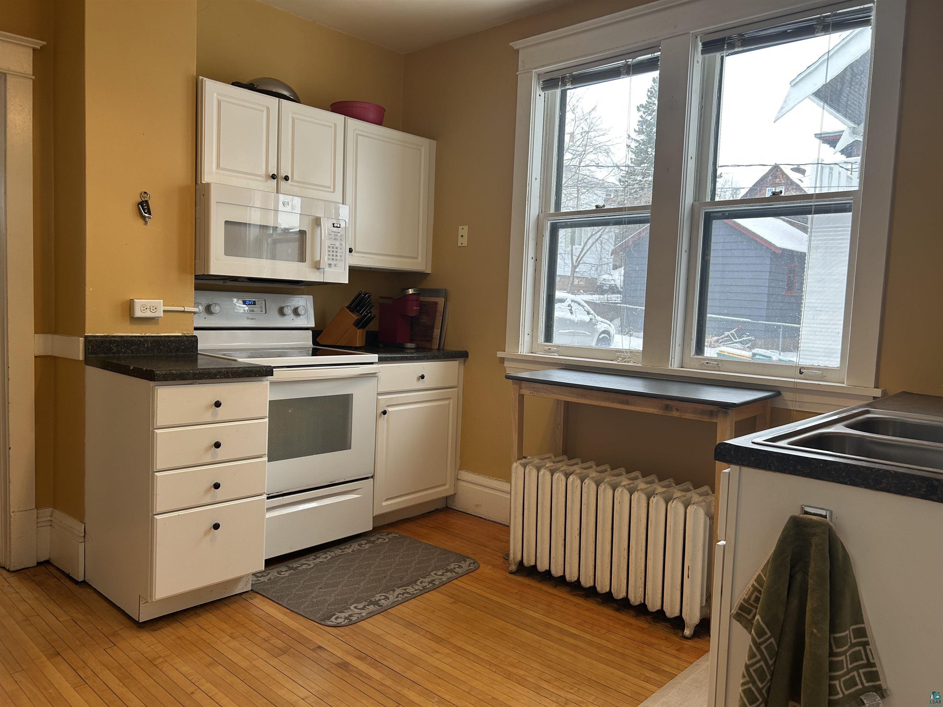 1723 East 4th Street Duluth, MN 55812 - Photo 10 of 47 Kitchen featuring dark countertops, white appliances, radiator, and white cabinetry