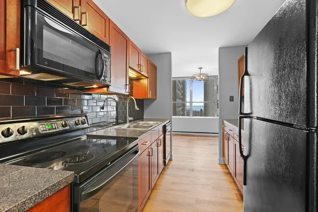 a kitchen with stainless steel appliances granite countertop a refrigerator a stove and a sink with wooden floor