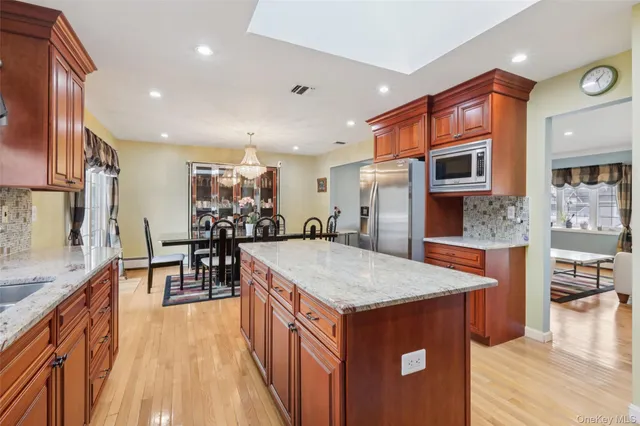 a kitchen with stainless steel appliances granite countertop a refrigerator a stove top oven a dining table and chairs with wooden floor