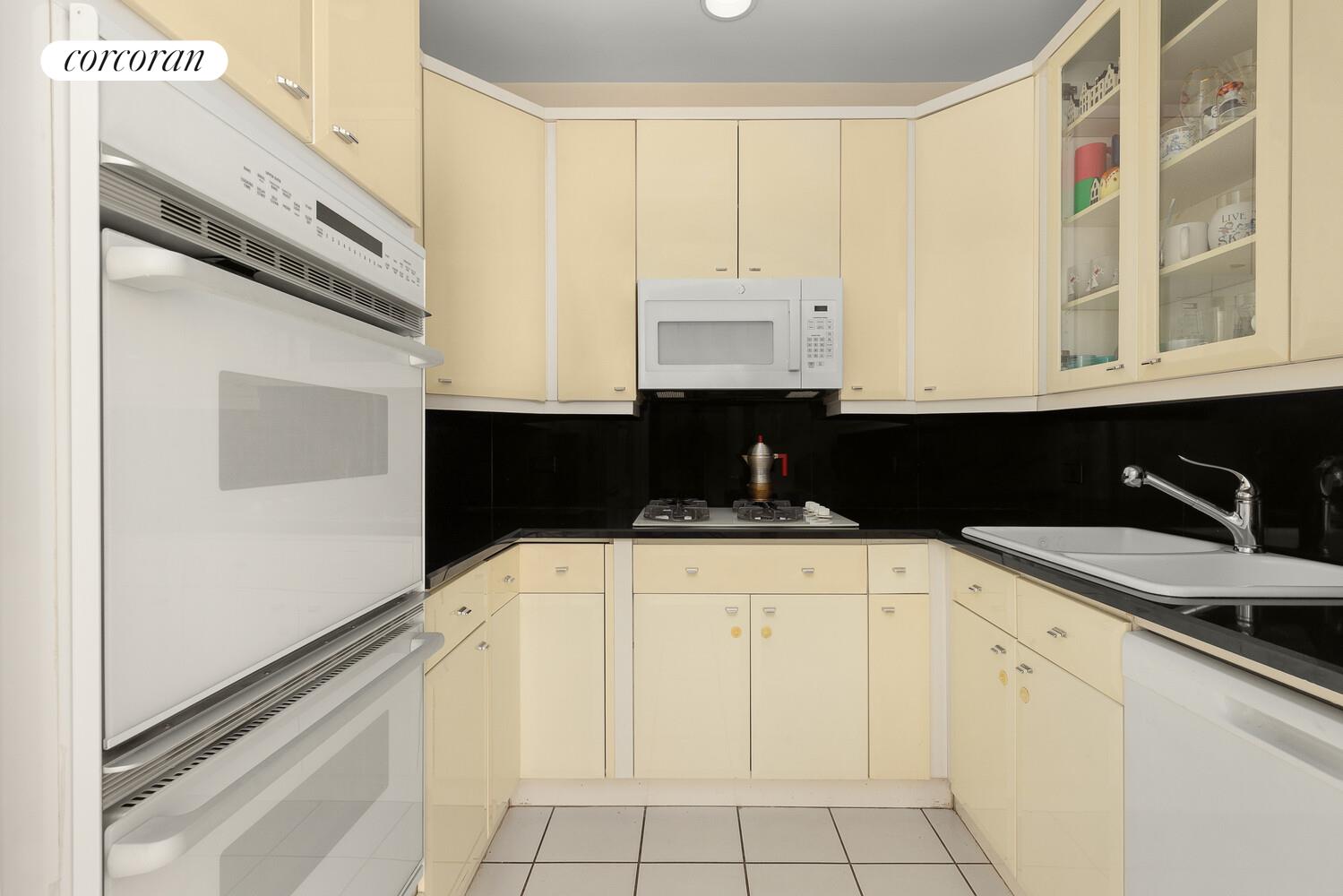 1 Central Park West, Unit 23C Manhattan, NY 10023 - Photo 8 of 10 a kitchen with granite countertop white cabinets and black appliances