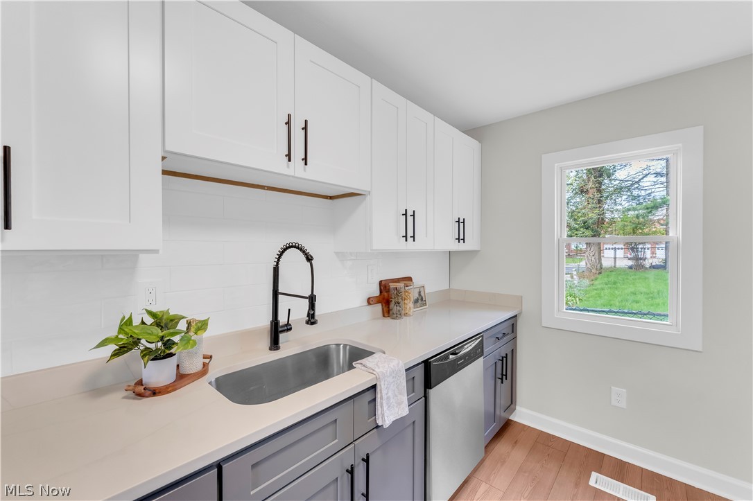 18155 Libby Road Maple Heights, OH 44137 - Photo 12 of 32 Kitchen featuring two-tone cabinetry with white upper cabinets and gray lower cabinets, light-toned countertops, a stainless steel undermount sink with a matte black gooseneck faucet, a white tile backsplash, and wood-finish flooring