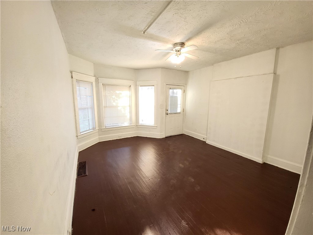 Spare room featuring ceiling fan, dark wood-style flooring, and a textured ceiling