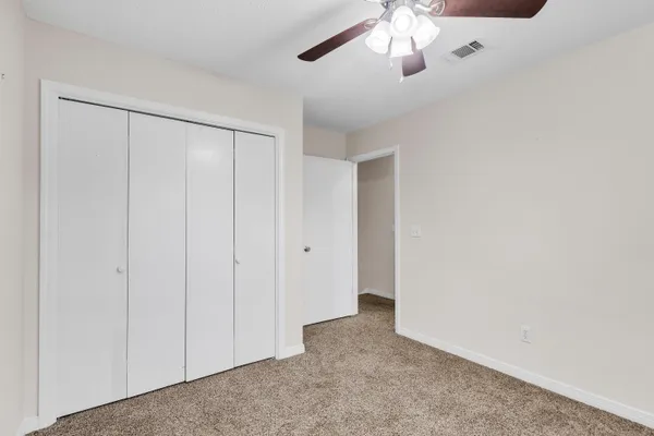 an empty room with a chandelier fan and closet area