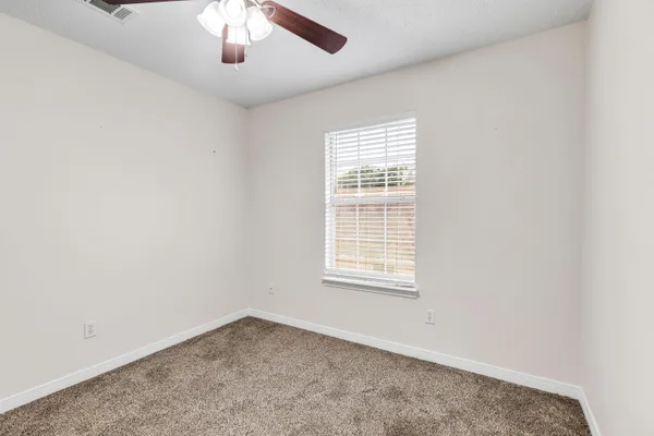 an empty room with a chandelier fan and windows