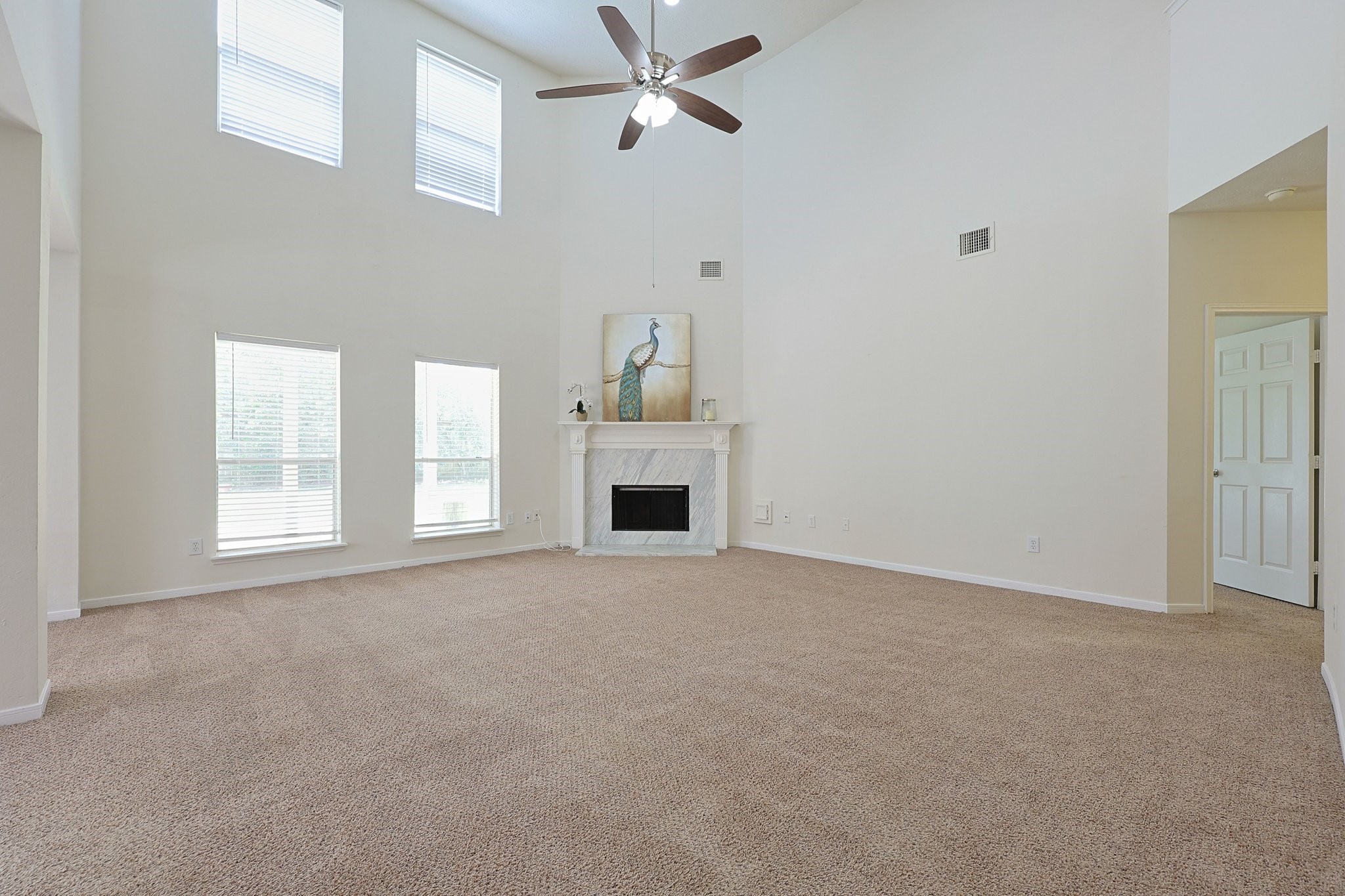 23019 Eastgate Village Drive Spring, TX 77373 - Photo 3 of 46 Spacious living room with high ceilings, large windows, and a ceiling fan. It features a central fireplace with a decorative mantle, creating a bright and inviting atmosphere.