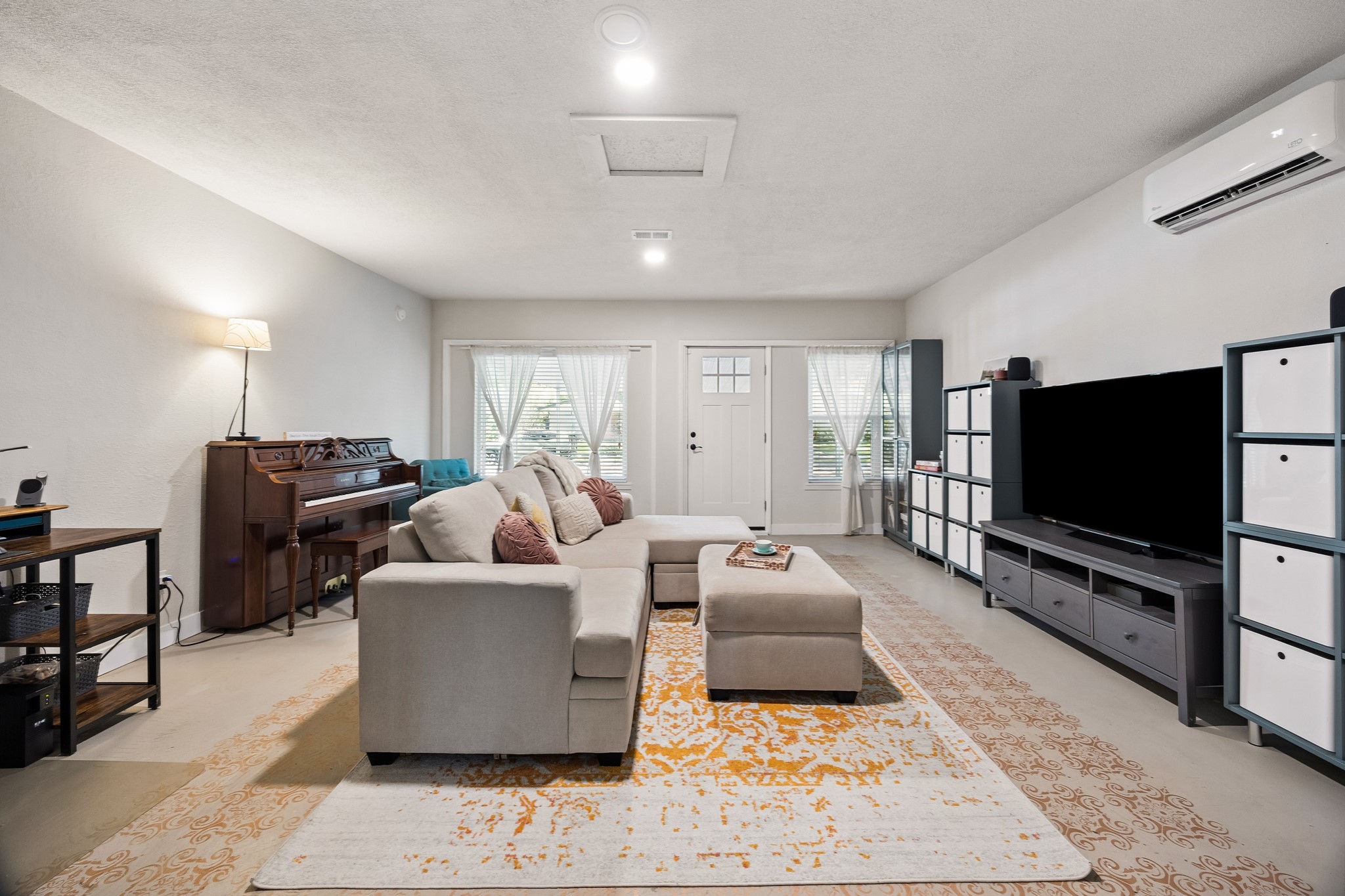 4514 Warm Springs Road Houston, TX 77035 - Photo 19 of 31 This spacious family room features a neutral color palette while natural light streams in through the windows. The gray painted concrete is accented with a stencil pattern in rose gold. The room's tempurature is cooled to perfection with a mini-split to the right. The door opens to the carport.