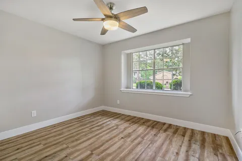 a view of an empty room with wooden floor and a ceiling fan