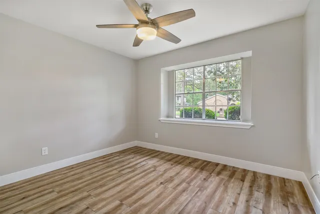 a view of an empty room with wooden floor and a ceiling fan