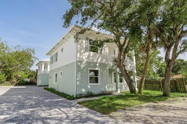 a view of a white house next to a yard with big trees