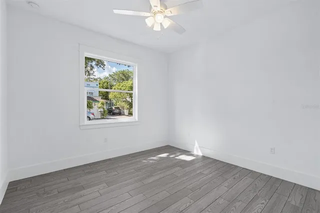 an empty room with wooden floor chandelier fan and windows