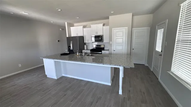 a room with stainless steel appliances kitchen island granite countertop a large counter top and wooden floors