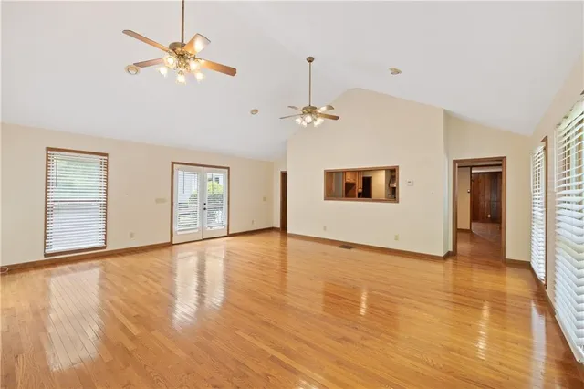 an empty room with wooden floor chandelier fan and windows