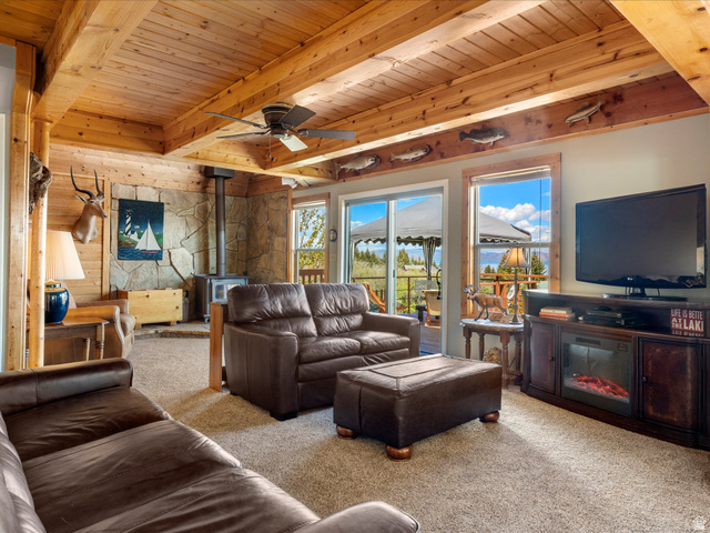 371 Lewis Loop, Unit 29 Fish Haven, ID 83287 - Photo 16 of 40 Living area featuring a wood-planked ceiling with exposed beams, a built-in stone accent wall with a wood-burning stove, and carpeted flooring