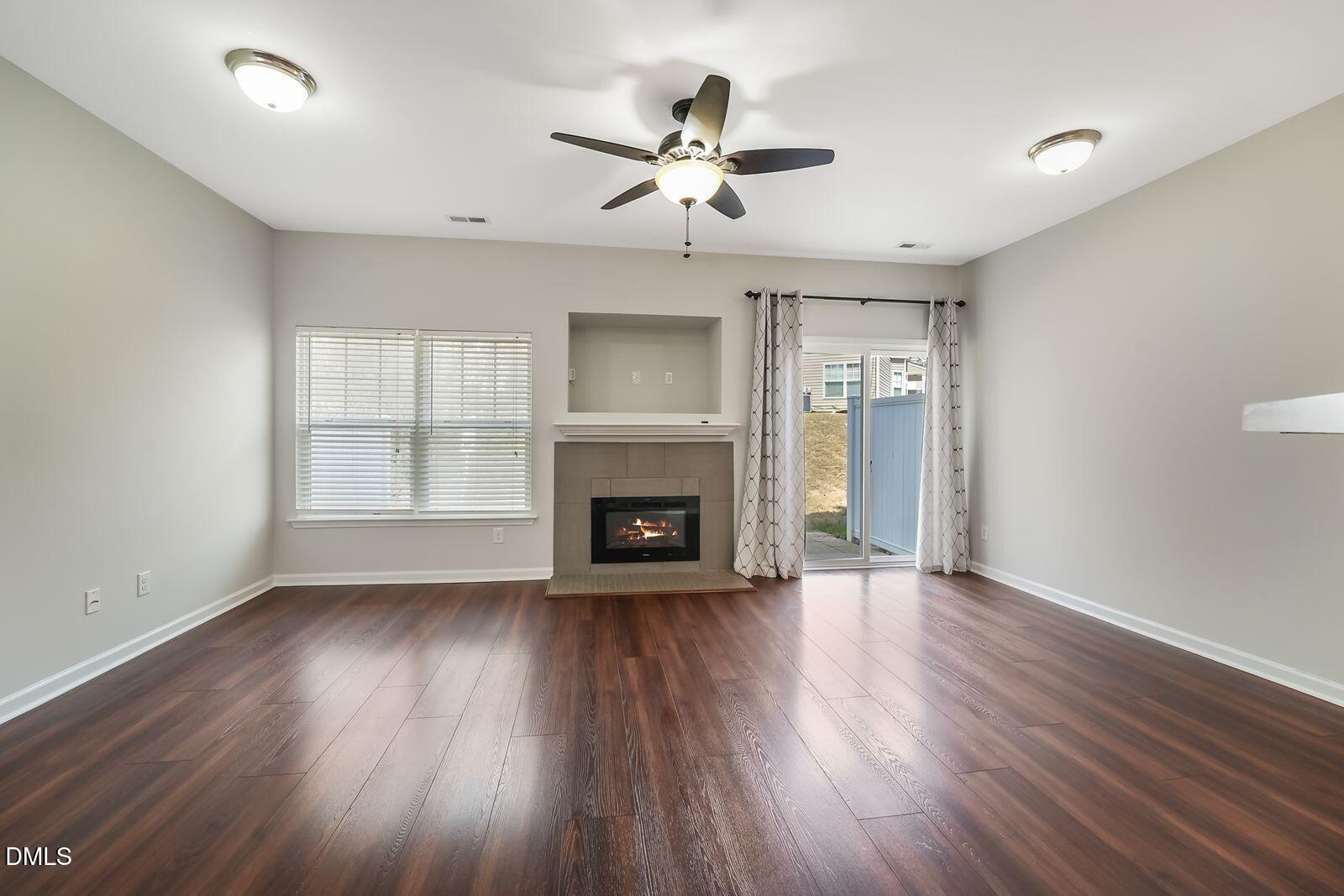 4909 Blue Rock Court Raleigh, NC 27610 - Photo 4 of 15 an empty room with wooden floor a fireplace a ceiling fan and windows