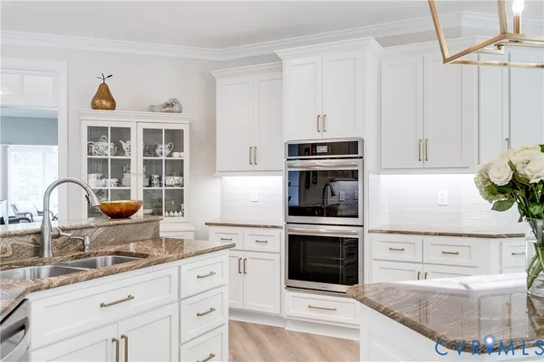 a kitchen with stainless steel appliances kitchen island granite countertop a refrigerator a stove top oven a sink dishwasher and white cabinets with wooden floor