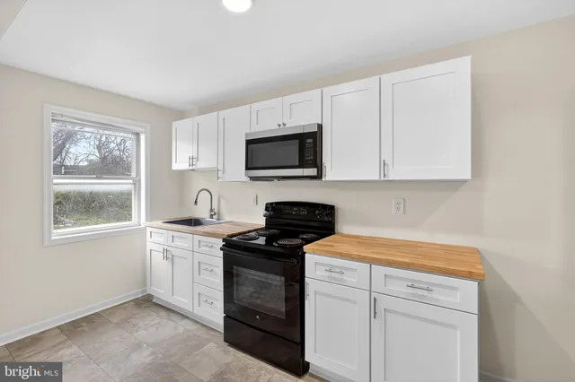 a kitchen with stainless steel appliances granite countertop white cabinets a sink a stove a window and a microwave