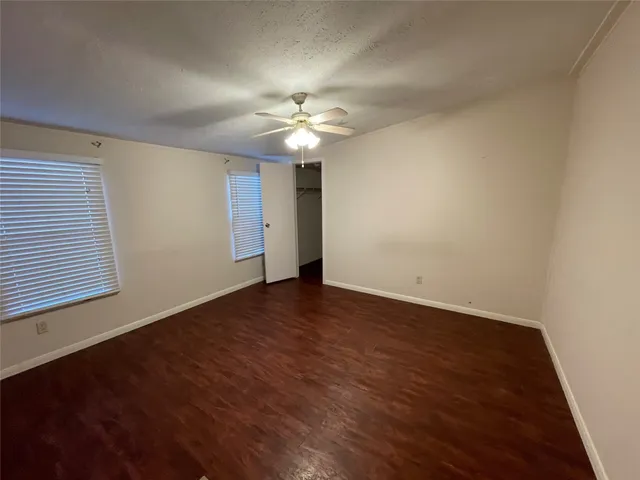 an empty room with wooden floor chandelier fan and windows
