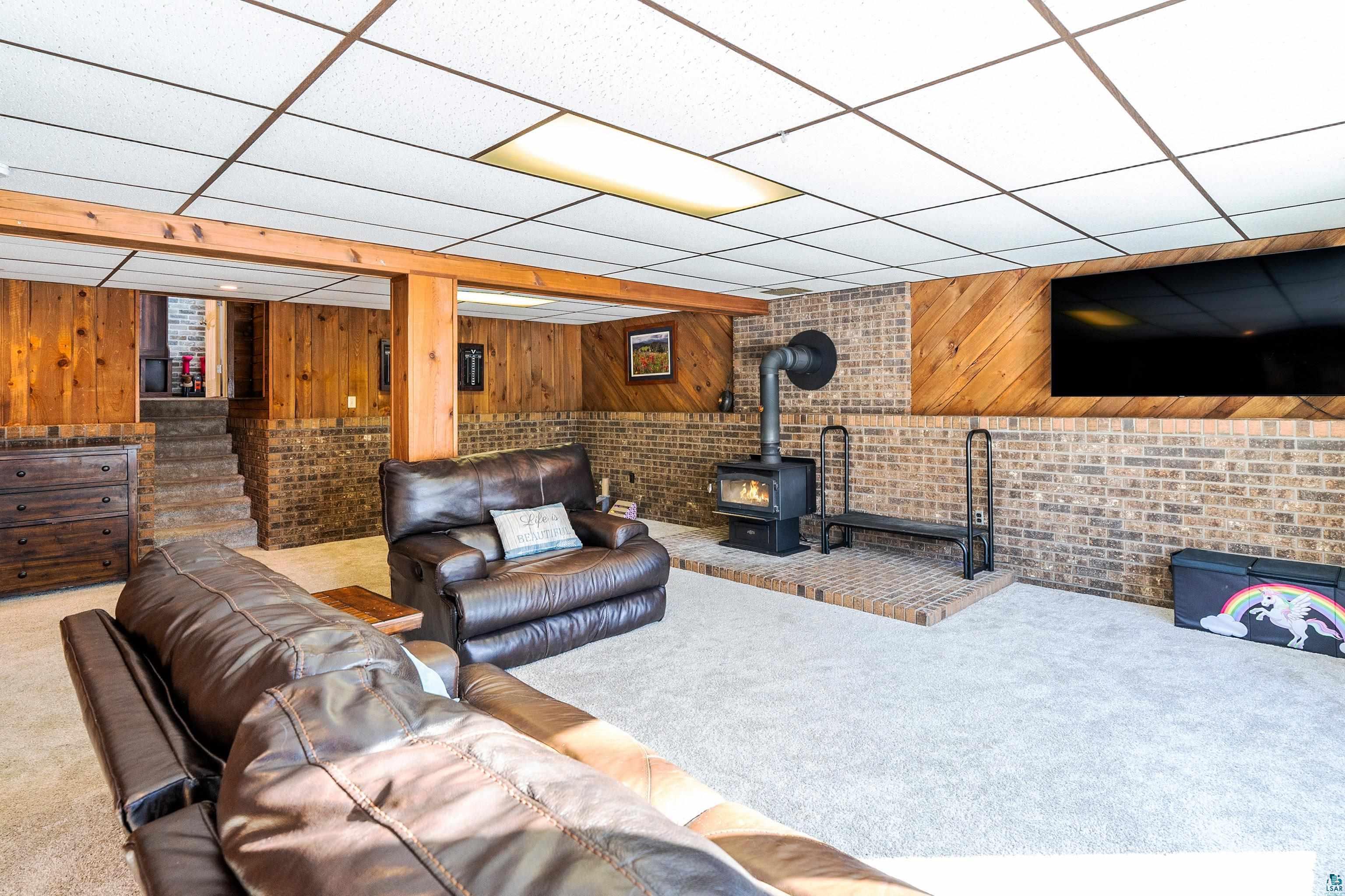 5947 East St Louis River Road Proctor, MN 55810 - Photo 24 of 47 Carpeted living room with a drop ceiling, a wood stove, brick wall, and wooden walls