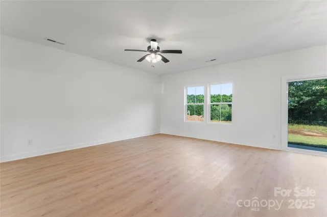 an empty room with wooden floor chandelier fan and windows