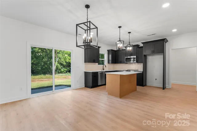 a large kitchen with kitchen island a large counter top a sink stainless steel appliances and cabinets