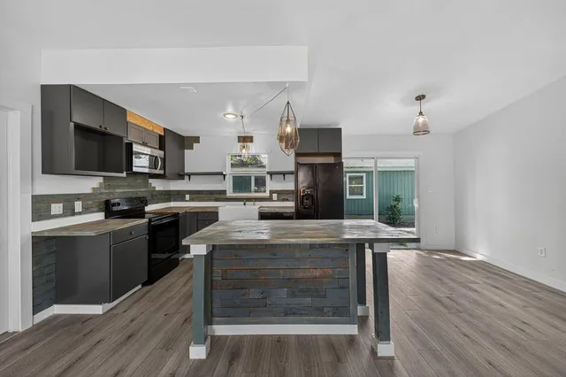 a kitchen with kitchen island granite countertop a stove top oven a sink dishwasher a dining table and chairs with wooden floor