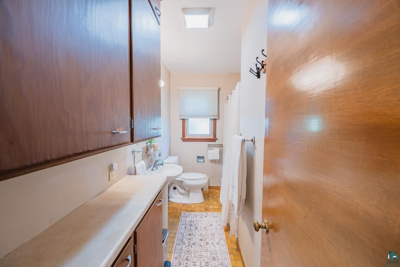 101 2nd Avenue North Biwabik, MN 55708 - Photo 17 of 44 Bathroom featuring a window, white roller shade, white toilet, and wood-finish door