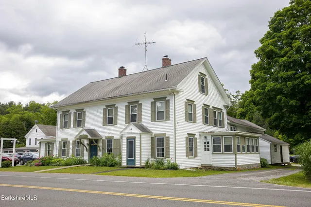 a view of a white house with a yard plants and large tree