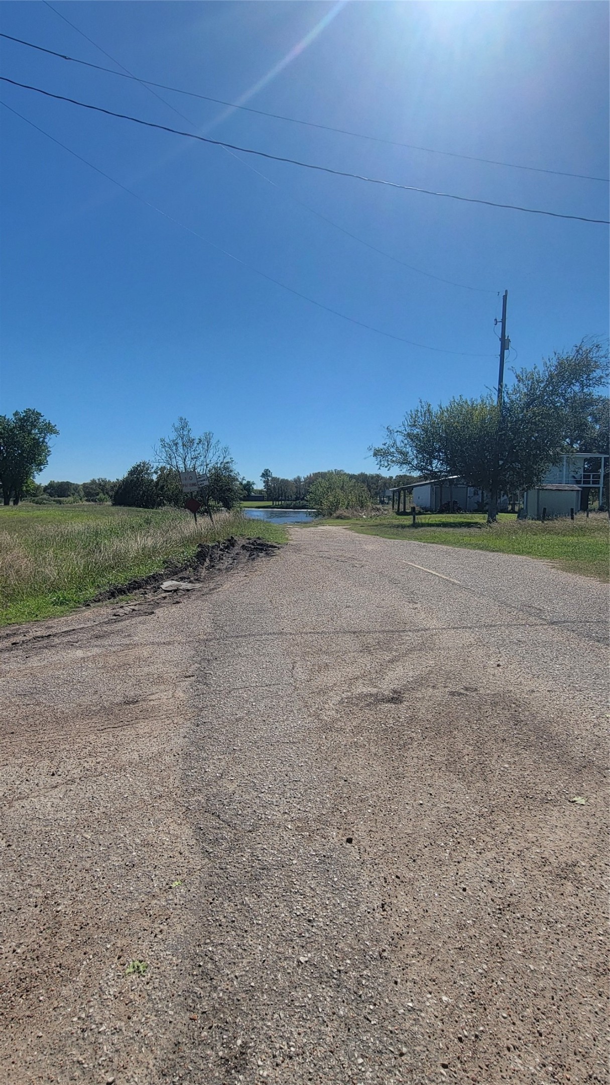 12018 Sandpiper Road Angleton, TX 77515 - Photo 40 of 48 A serene, rural setting with a quiet paved road, surrounded by open grassy areas and scattered trees. A small water feature is visible in the distance, and there are a few structures nearby. Ideal for those seeking a peaceful environment.