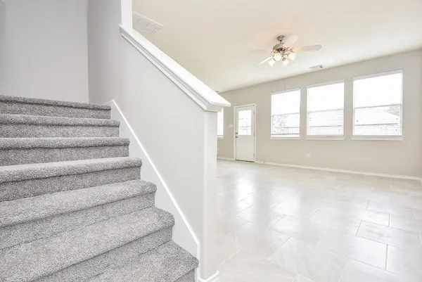 a view of an empty room with stairs and chandelier fan